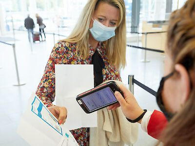 Two women with mouth-to-nose coverings. One scans the ticket of the other via smartphone.