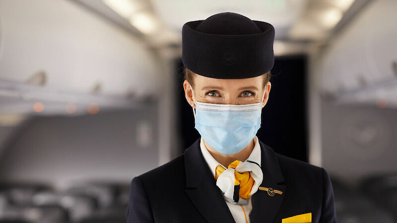 Flugbegleiterin der Lufthansa in Uniform und mit Mund-Nasen-Bedeckung