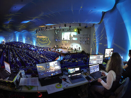 View into the control room of an event at Congress Center Düsseldorf with stage and participants in the audience.