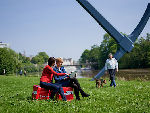 Zwei Frauen auf roten Sitzwürfeln mit Laptop an der Spitzhacke in Kassel