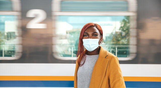 Frau, die mit dem Zug reist, respektiert die Regeln und trägt eine chirurgische Gesichtsmaske am Bahnhof.
